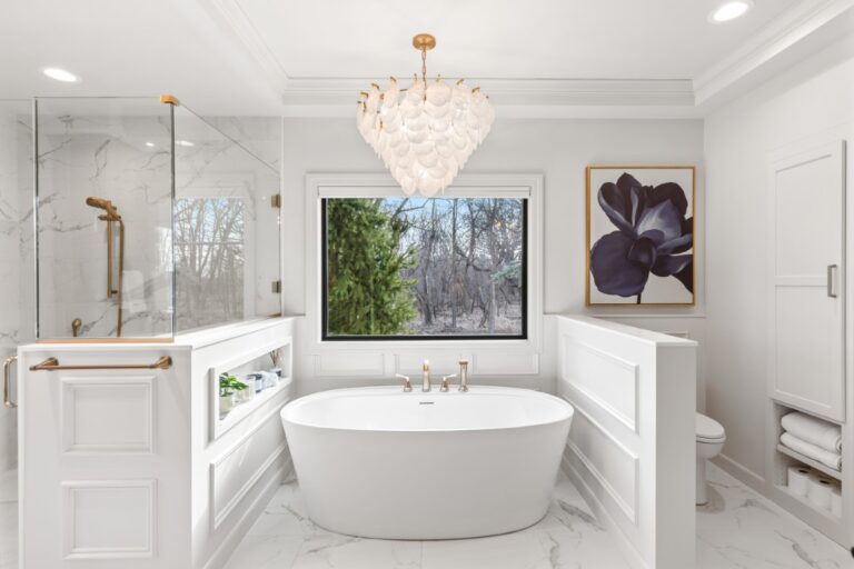 Modern luxury bathroom with white oval freestanding tub, marble tile walls, chandelier, and botanical wall art