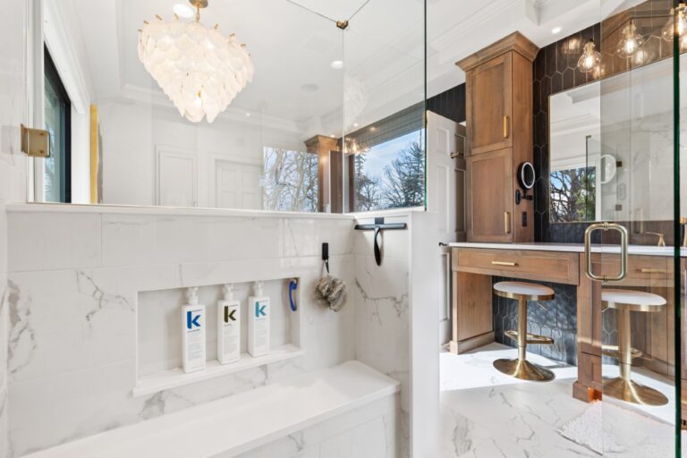 Modern bathroom with white marble countertops, wooden cabinetry, pendant lighting, and mirrored vanity