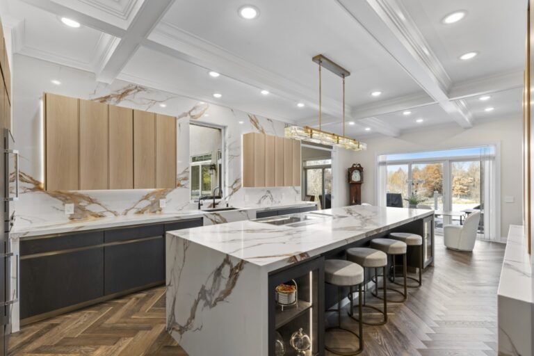 Modern kitchen with marble island, stainless steel appliances, light wood cabinets, and coffered ceiling with recessed