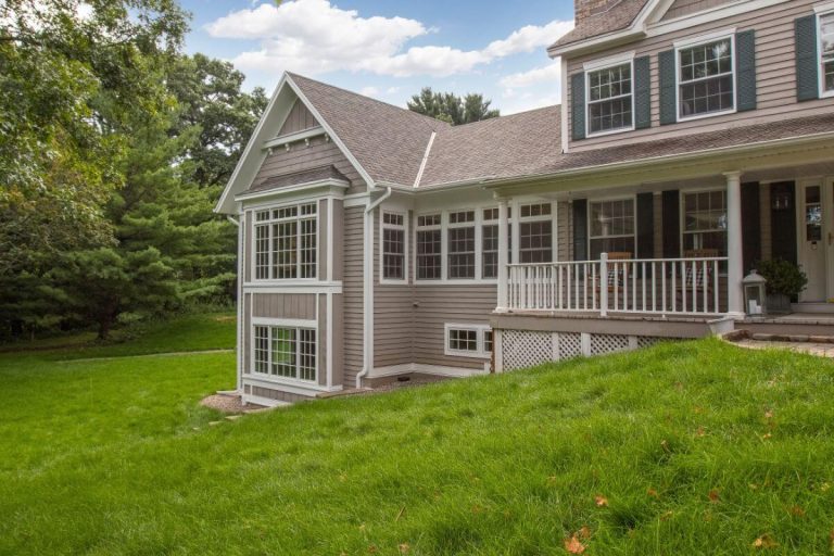 Two-story gray residential home with white trim, covered porch, and manicured lawn surrounded by trees