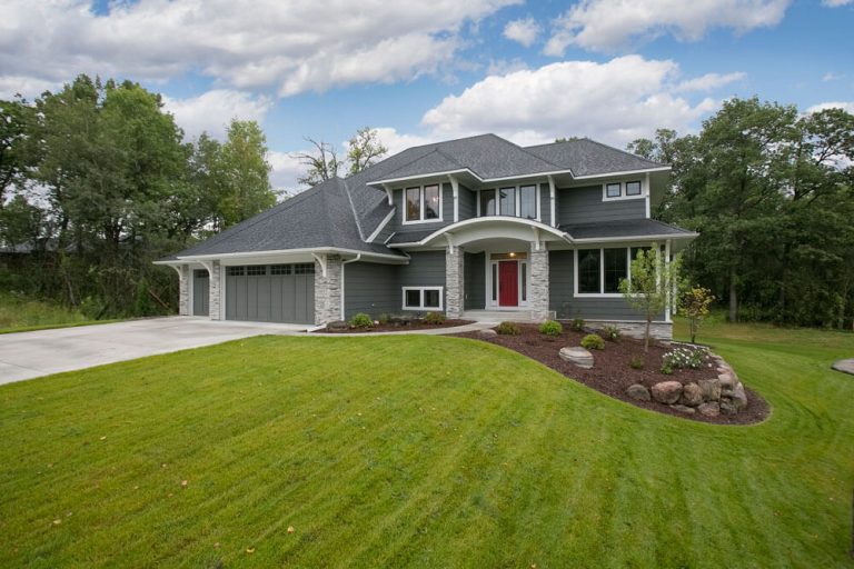 Modern two-story home with gray siding, red door, attached garage, manicured lawn and landscaped flower beds