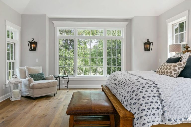 Bright bedroom with large windows, wooden bed, armchair, and hardwood flooring