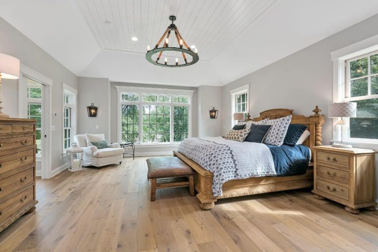 Spacious master bedroom with wooden bed, natural wood flooring, large windows, dresser, and contemporary lighting