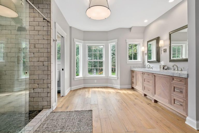 Luxury bathroom with wood flooring, dual vanity, large windows, glass walk-in shower with subway tile, and round ceiling