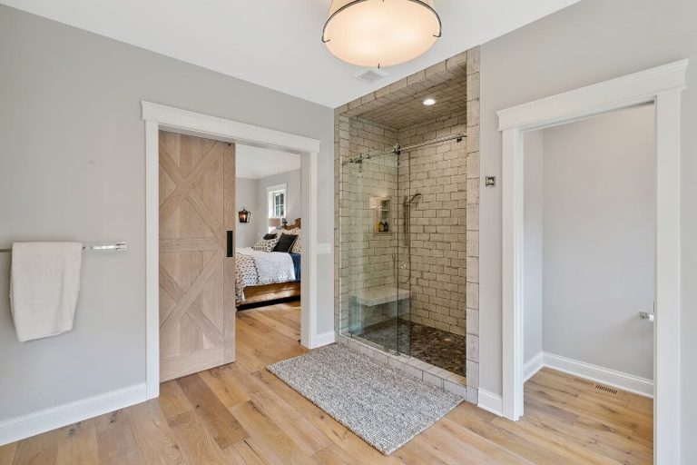 Modern primary bathroom with walk-in shower, double vanity, wood flooring, and neutral decor
