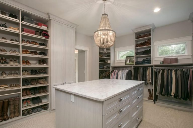 Luxury walk-in closet with white cabinetry, organized shelving, island with drawers, pendant lighting, and clothing racks