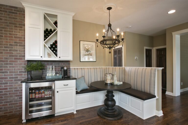 Modern kitchen nook with white cabinetry, black countertops, built-in wine cooler, and brick accent wall with pendant