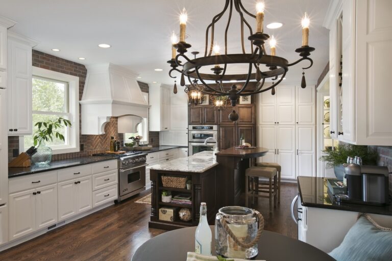 Modern kitchen with white cabinets, dark island, chandelier lighting, and hardwood floors