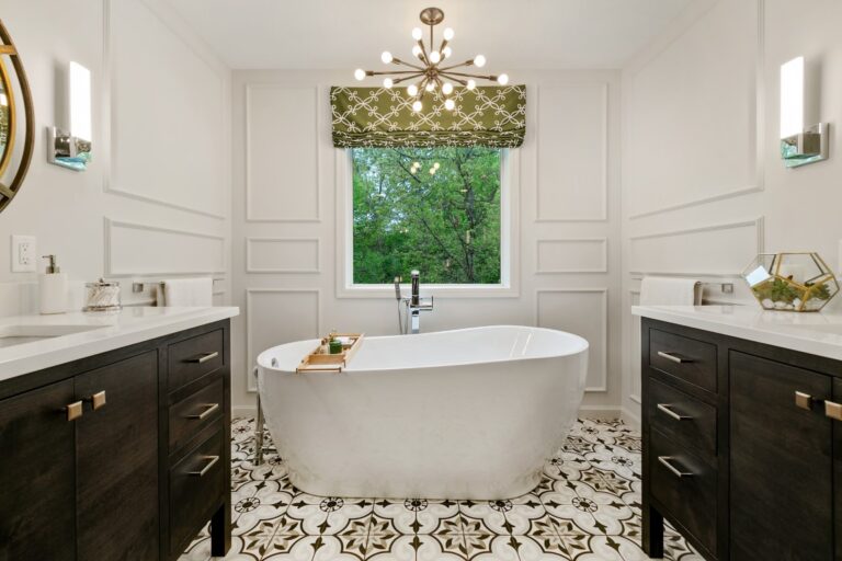 Luxury bathroom with white walls, freestanding white tub, black vanities, marble patterned floor, and brass pendant light