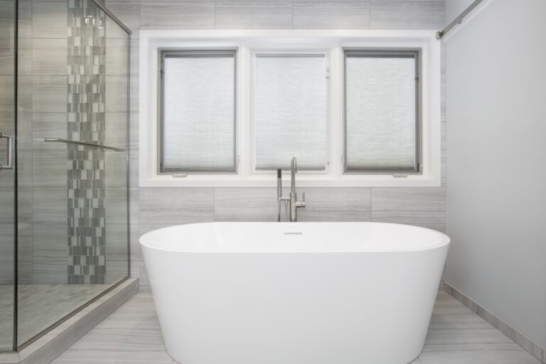 Modern bathroom with freestanding white soaking tub, dual sink vanity, glass shower enclosure, and three windows