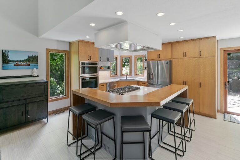 Modern kitchen with wood cabinetry, large island with seating, stainless steel appliances, and recessed lighting