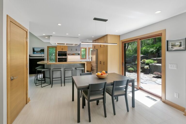 Modern kitchen and dining area with wood cabinets, black dining table, and view to backyard patio