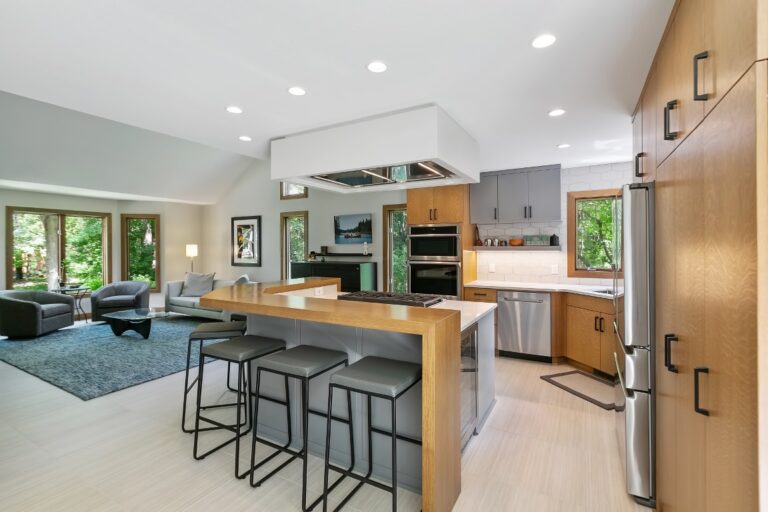 Modern kitchen with wooden island, bar seating, stainless steel appliances, and open living area with teal seating
