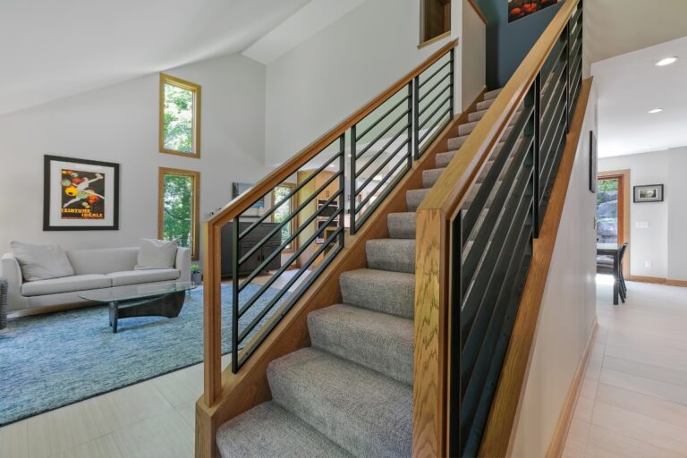 Modern staircase with wooden railings and black metal balusters leading to upper level in bright contemporary home interior