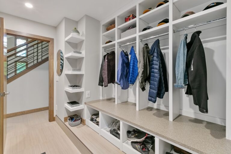 Modern mudroom with white built-in shelving, hanging jackets, storage cubbies, and wooden framed doorway