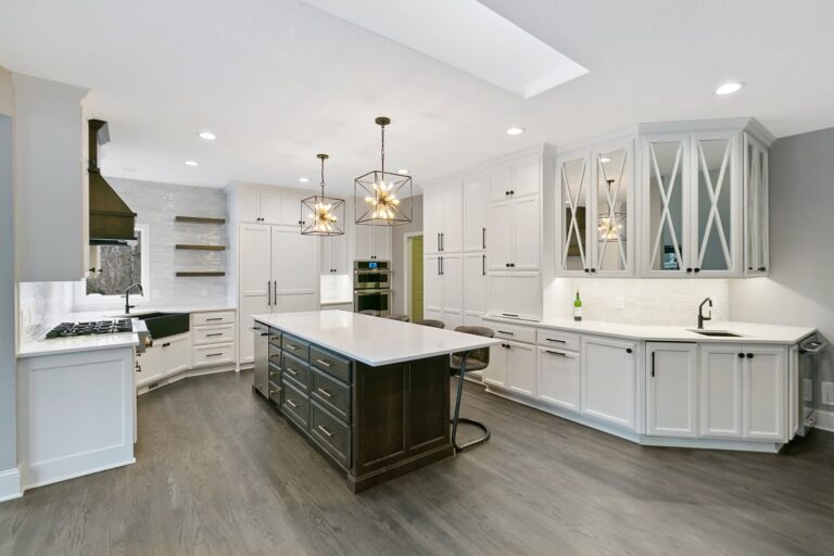Modern luxury kitchen with white cabinetry, dark island, marble countertops, and pendant lighting