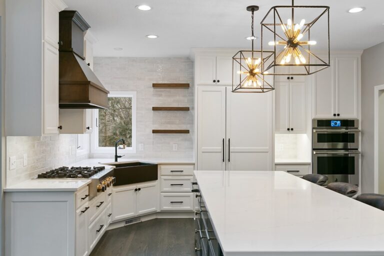 Modern kitchen with white cabinetry, gold pendant lights, stainless steel appliances, and white quartz island countertop