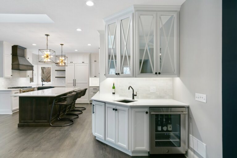 Modern kitchen with white cabinetry, marble countertop, glass-front upper cabinets, and black island in background with
