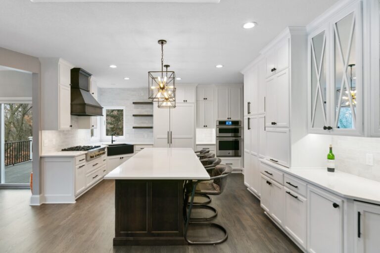 Modern kitchen with white cabinetry, dark island with seating, stainless steel appliances, and pendant lighting