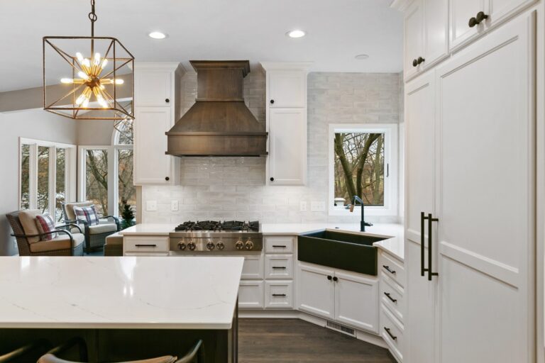 Modern white kitchen with island, stainless steel range hood, pendant lighting, and marble countertops