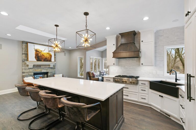 Modern kitchen with white cabinetry, dark island, pendant lighting, and stainless steel appliances