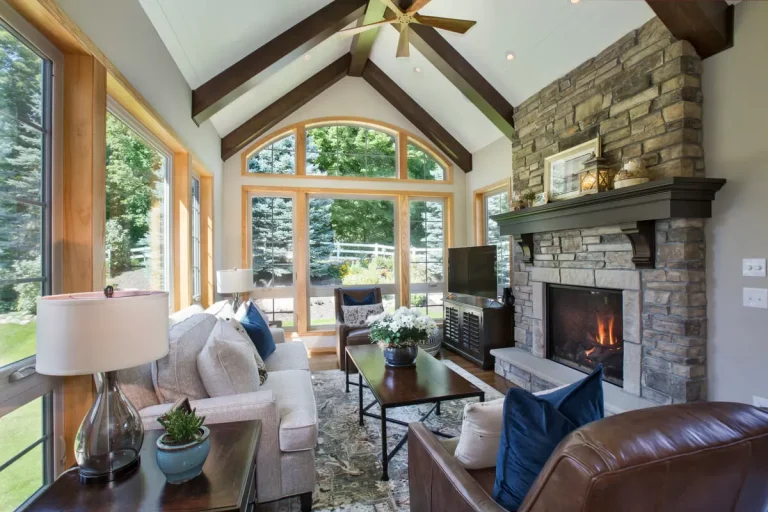 Modern living room with vaulted ceilings, stone fireplace, leather seating, and expansive windows overlooking green landscape