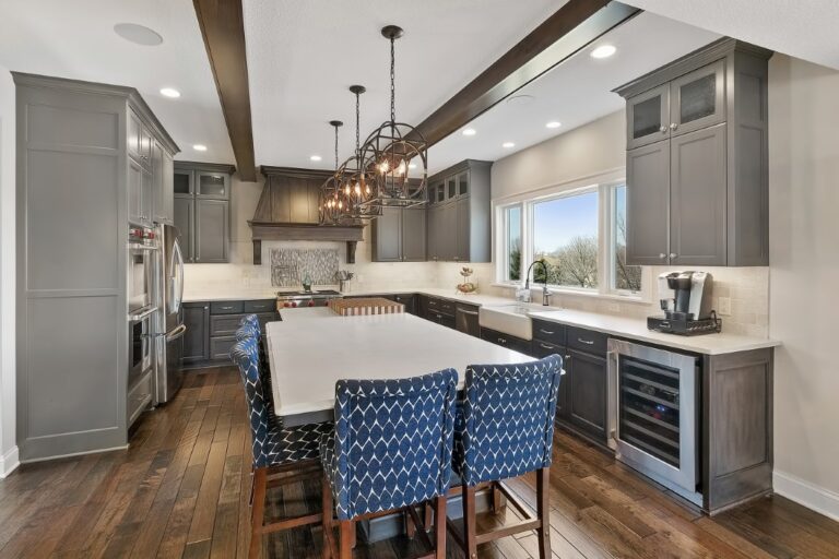Modern kitchen with white island, blue upholstered chairs, gray cabinets, and stainless steel appliances