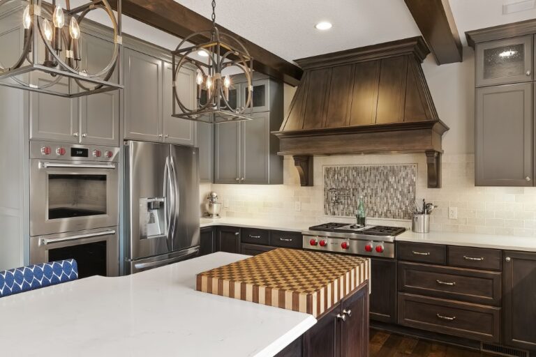 Modern kitchen with gray cabinetry, stainless steel appliances, white countertop island, and bronze range hood