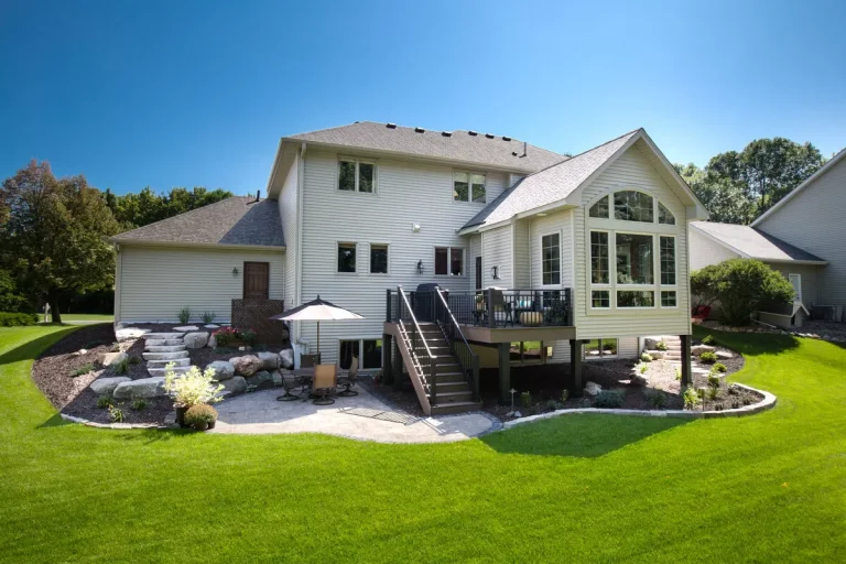 Large white two-story house with deck and patio surrounded by manicured lawn and landscaping