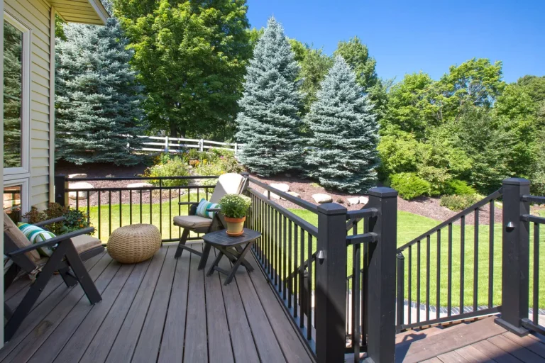 Spacious composite deck with black railings, lounge chairs, and landscaped yard with evergreen trees