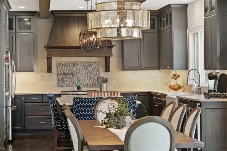 Modern kitchen with dark gray cabinets, white marble countertops, and a dining table with upholstered chairs