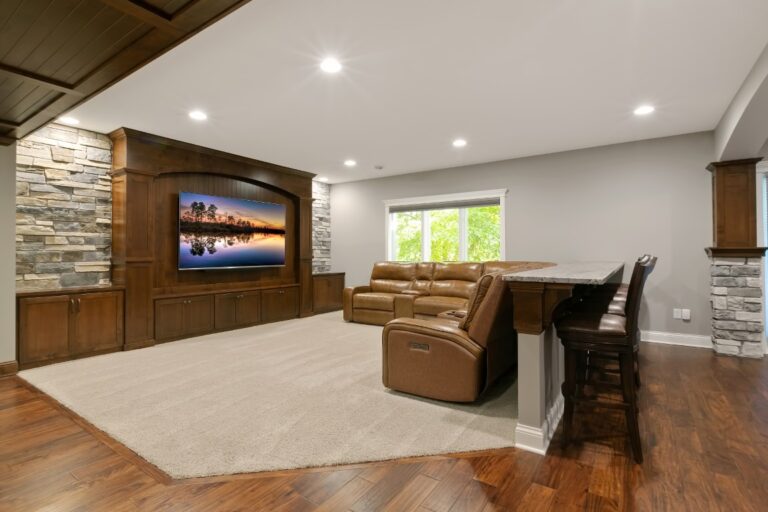 Modern basement entertainment room with wood cabinetry, leather seating, bar area, and recessed lighting
