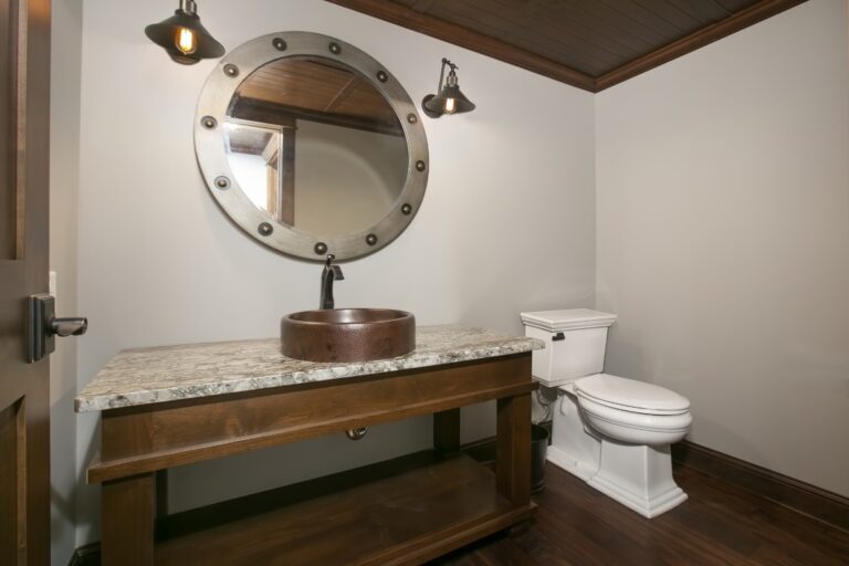 Rustic bathroom vanity with granite countertop, round mirror, and toilet fixtures