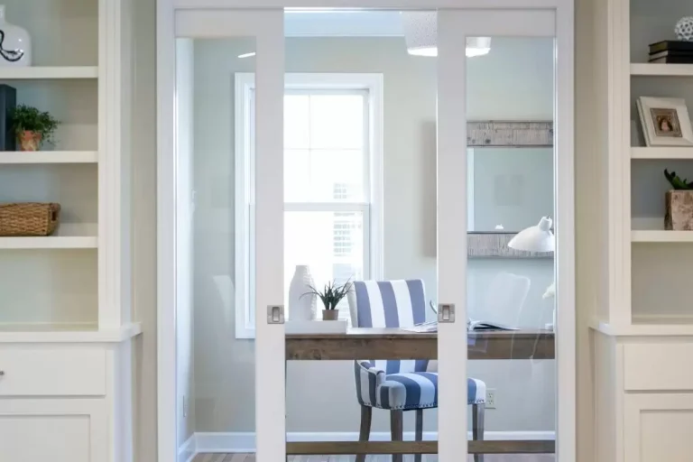 Modern home office with glass doors, white shelving, desk, and blue striped chair