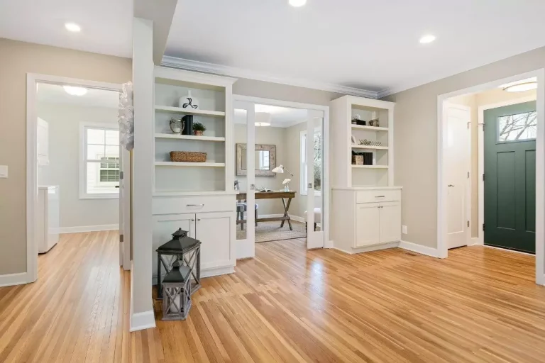 Bright modern entryway with wood flooring, white built-in shelving, green front door, and glass shower enclosure
