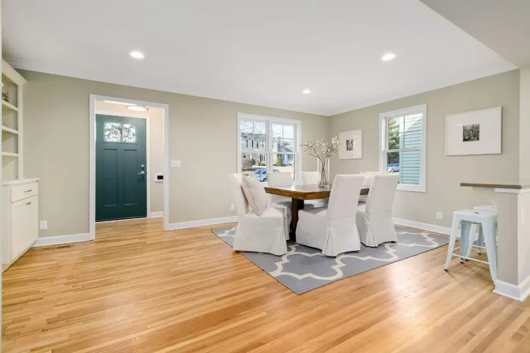 Bright open concept living space with hardwood floors, dining table, armchair, built-in shelving, and dark teal door