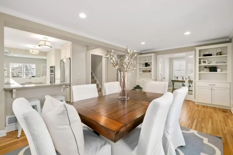 Elegant dining room with wooden table, white upholstered chairs, and built-in cabinetry with hardwood flooring
