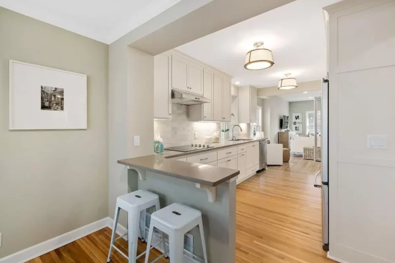 Modern kitchen with gray island, white bar stools, stainless steel appliances, and wooden flooring