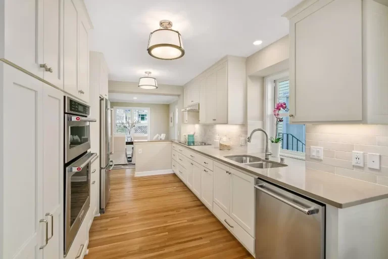 Modern white kitchen with stainless steel appliances, white cabinetry, quartz countertops, and hardwood flooring