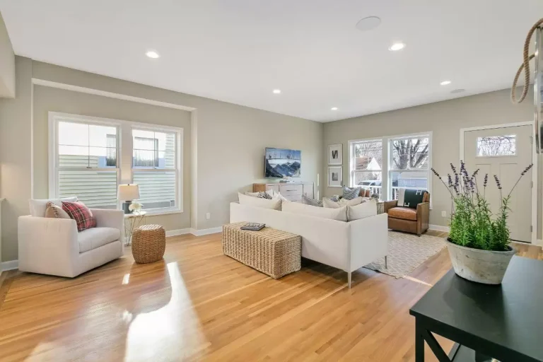 Bright modern bedroom with hardwood floors, white furniture, large windows, and neutral décor accents