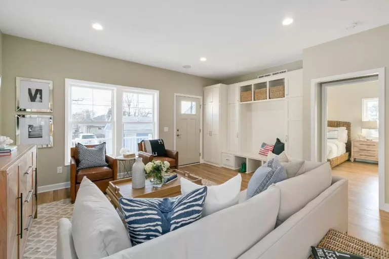 Modern living room with beige sectional sofa, wooden desk, desk chair, and doorway leading to bedroom