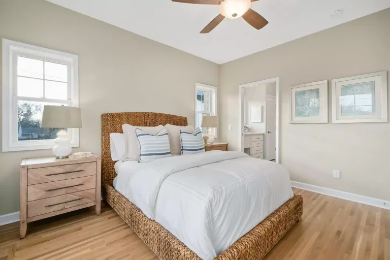 Bright master bedroom with wooden bed frame, matching nightstands, white bedding, hardwood floors, and ceiling fan