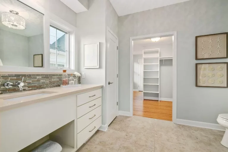 Modern bathroom with white vanity, double sink, marble backsplash, and open walk-in closet with wooden flooring
