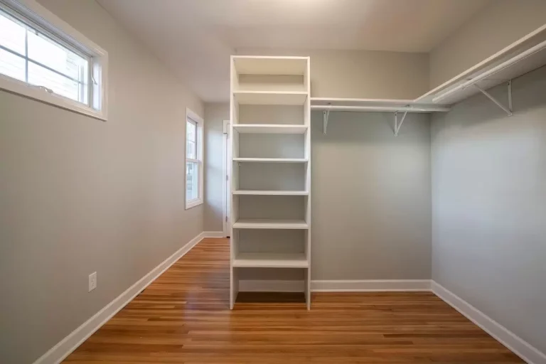 Empty walk-in closet with wooden floor, white shelving unit, and natural light from window