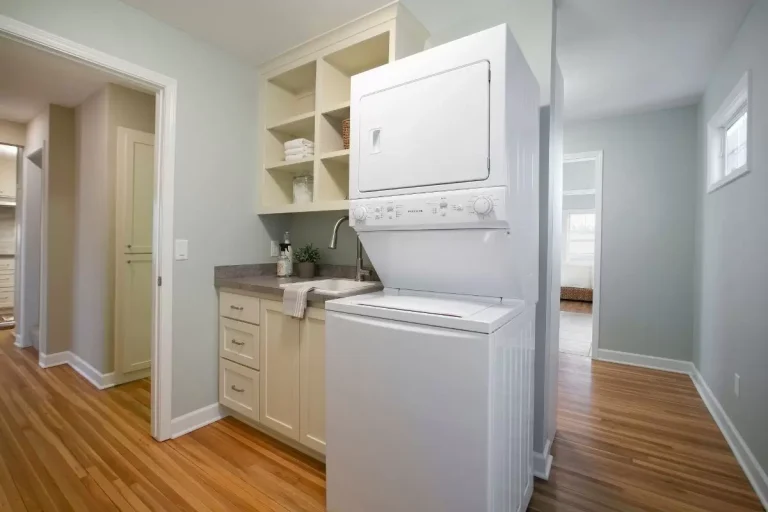 Modern laundry room with stacked white washer and dryer, wooden cabinets, and shelving against white walls