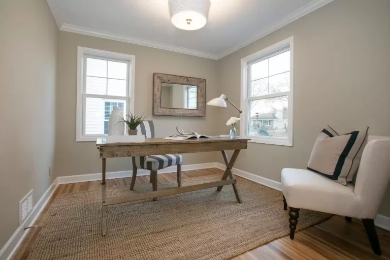 Bright home office with desk, chair, accent chair, mirror, windows, and neutral decor