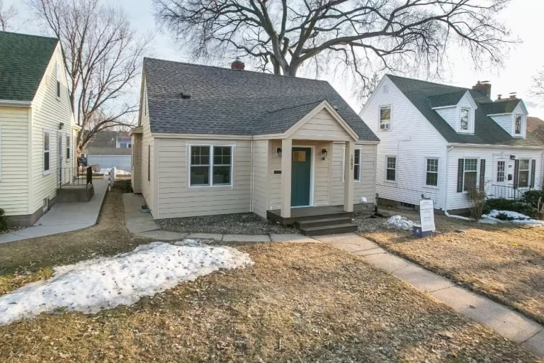 Single-story beige house with front porch and bare trees in winter setting with patchy snow on lawn