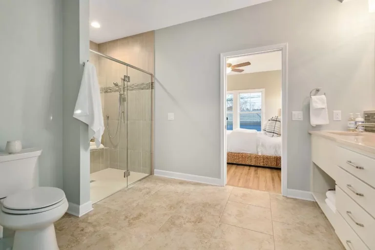 Modern bathroom with walk-in shower, toilet, vanity, and view into bedroom with hardwood floors