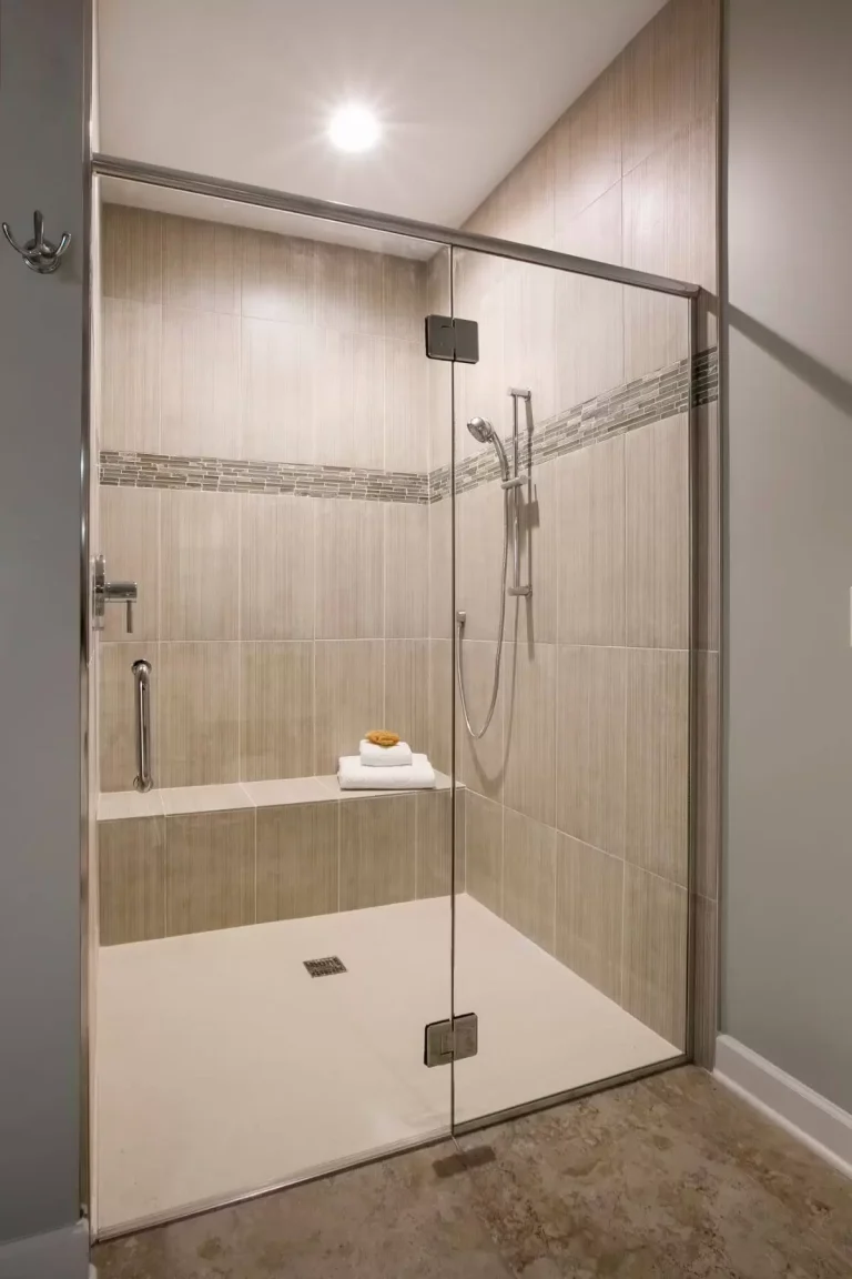 Modern walk-in shower with glass enclosure, bench seating, and neutral tile walls