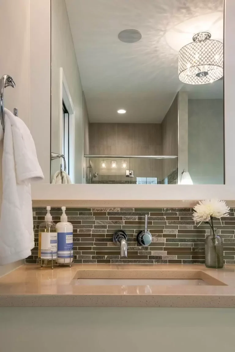 Modern bathroom vanity with brick tile backsplash, wooden countertop, and white sink under a large mirror with lighting